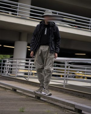 A man in a black and green techwear outfit consisting of Arc'teryx Sinsolo Bucket Hat, Nemen Techwear Jacket, Nemen Techwear Shirt and ACRONYM P30A-DS Techwear Pants and Asics Techwear Sneakers