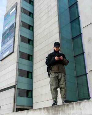 Techwear.Germany aka Janek next to a big futuristic building in Copenhagen in a Techwear outfit consisting of North Face Cap, ACRONYM J1WTS-GT Techwear Jacket, ACRONYM P30A-DS Techwear Pants, Equip Techwear Messenger Bag and Asics Gel Nimbus9 Shoes
