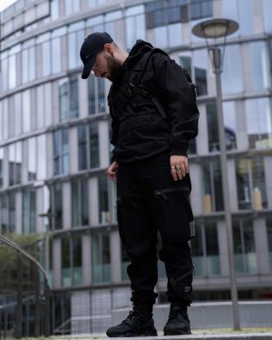 A man standing in front of a futuristic building in a techwear outfit consisting of a GStar Raw overshirt, GStar Raw RCT techwear cargo pants and Nike Air Huarache techwear shoes