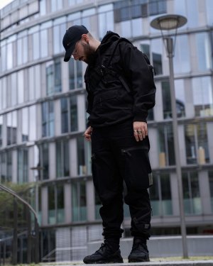 Ein Mann stehend vor einem futuristischen Gebäue in einem Techwear Outfit bestehend aus einem GStar Raw Overshirt, einer GStar Raw RCT Techwear Cargohose und Nike Air Huarache Techwear Schuhen