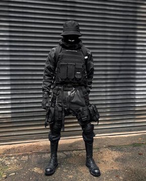 A man in an all-black warcore outfit with plate vest, magazine pouches, warcore pants with lots of accessories and mask